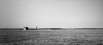 Black and white photograph of a farmhouse and windmill on a wide plain, Las Vegas, NM, architectural and landscape photography by Tony Sanders